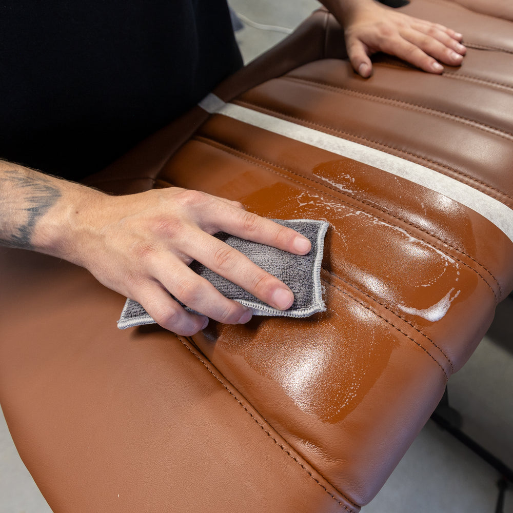 Leather Soft Cleaner being worked into a brown leather seat with a cleaning pad